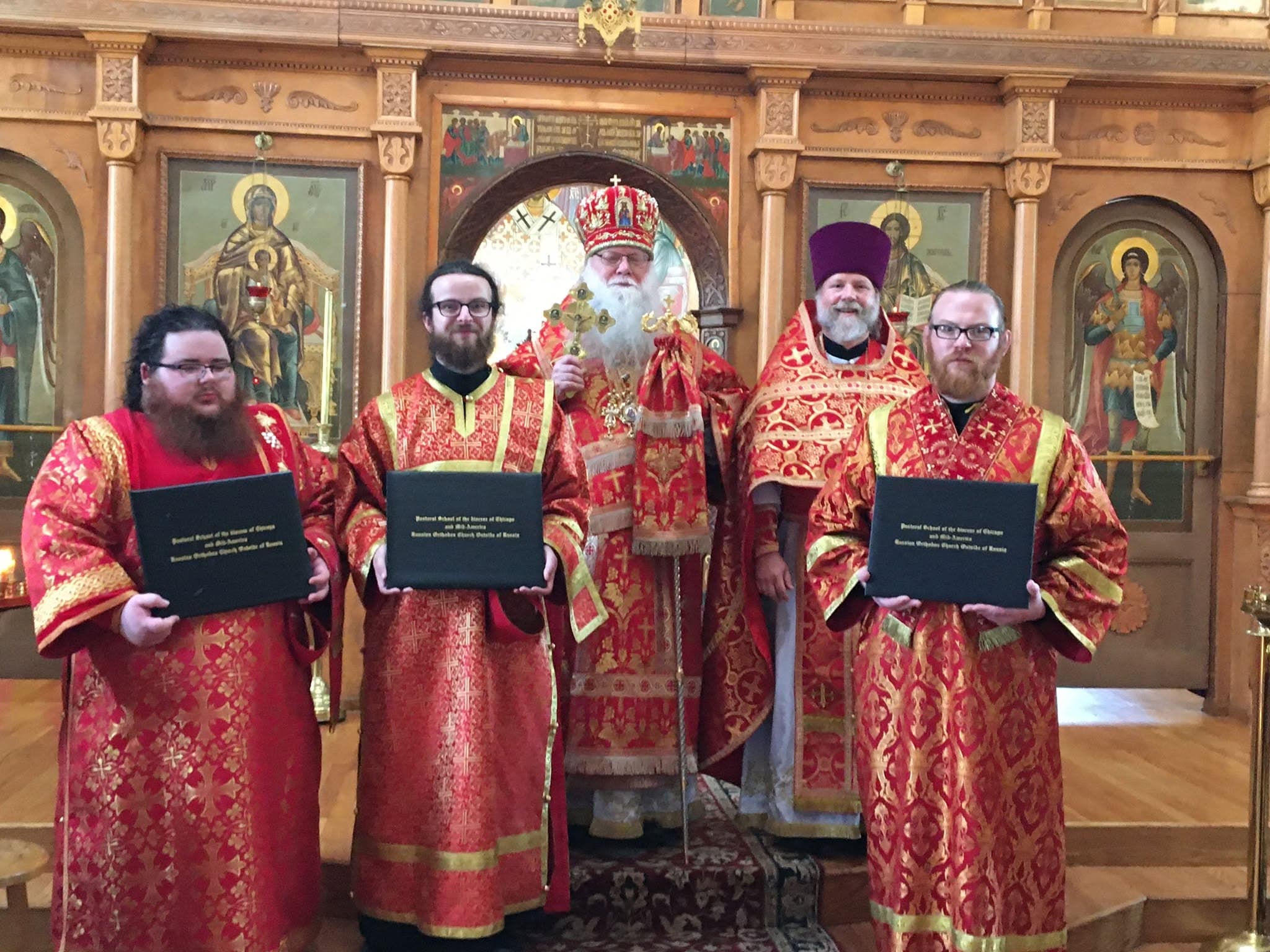 Выпускники в красных облачениях с дипломами